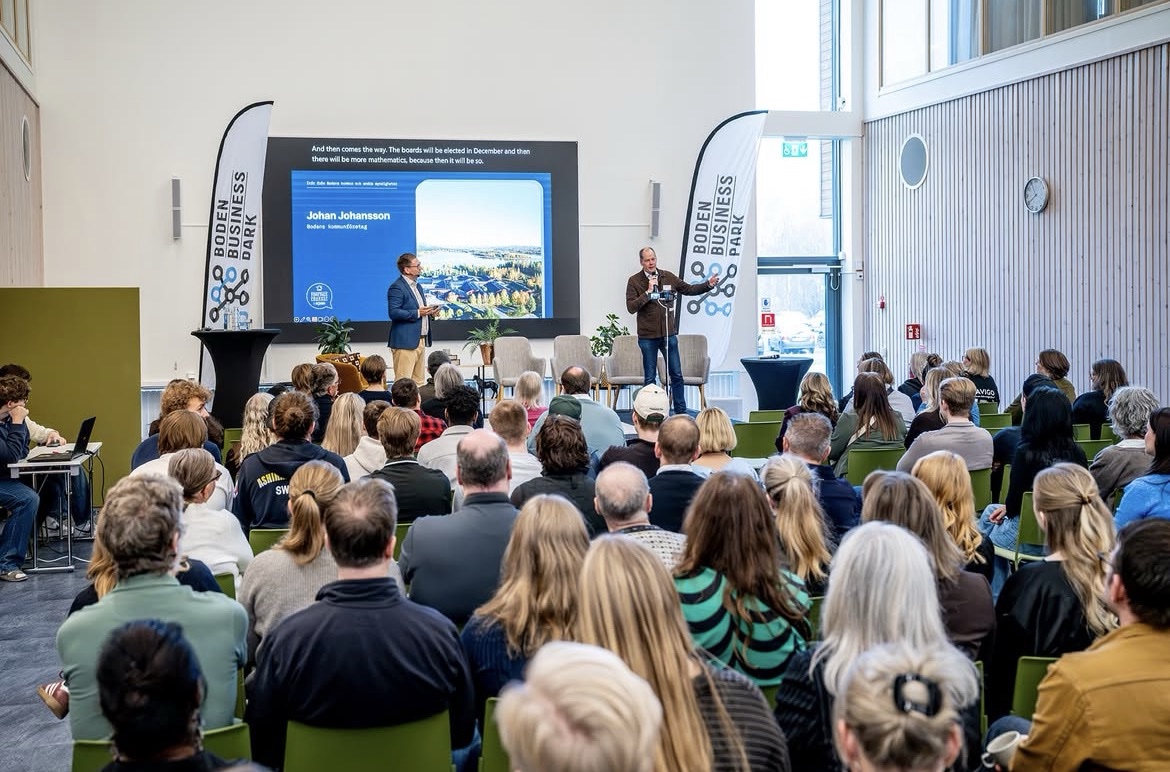Publik på ett evenemang i Boden Business Park, med talare på scen och presentation på storbildsskärm
